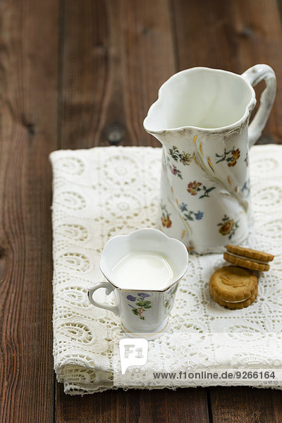 Tasse Milch,  Milchkanne und Kekse auf weißer Tischdecke