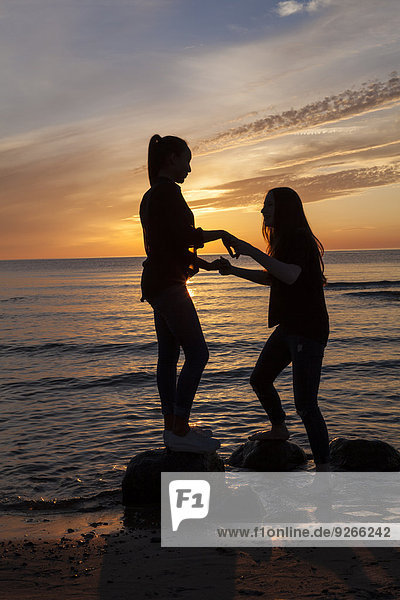 Deutschland  Rügen  Zwei junge Freundinnen am Strand bei Sonnenuntergang