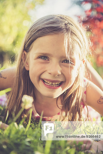 Porträt eines lächelnden kleinen Mädchens auf einer Wiese im Garten liegend