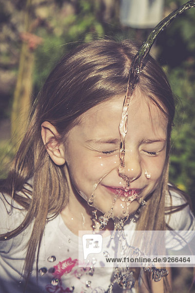 Kleines Mädchen  das sein Gesicht mit einem Wasserstrahl erfrischt.