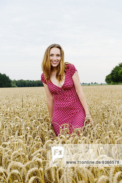 Porträt einer lächelnden jungen Frau in einem Getreidefeld stehend