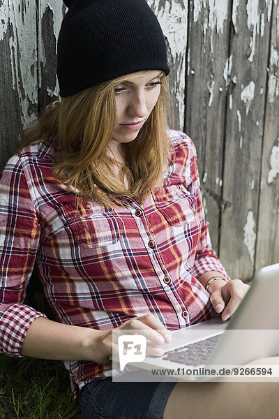 Portrait einer jungen Frau mit Laptop vor einer Holzwand