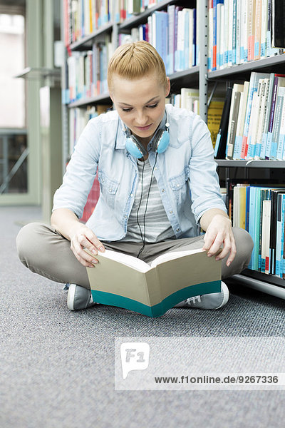 Student in a university library sitting on floor reading book