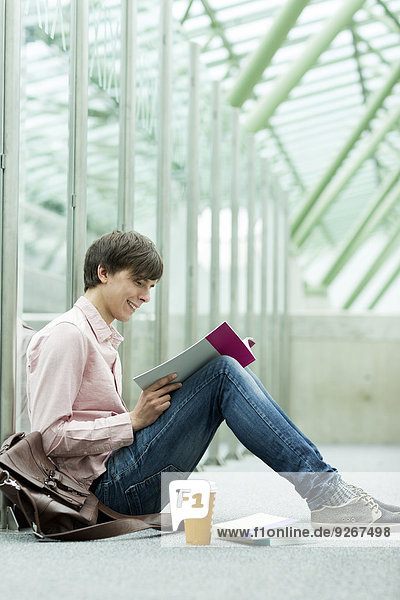 Student in einer Universitätsbibliothek sitzend auf dem Boden Lesebuch