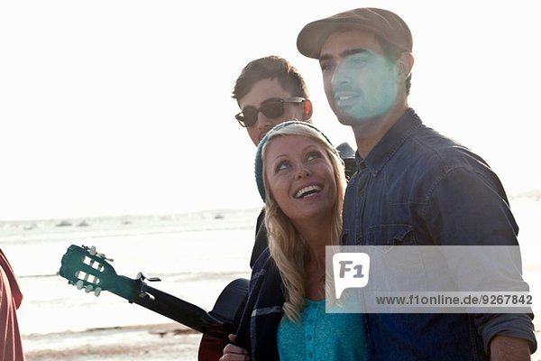 Three adult friends with acoustic guitar on Bournemouth beach  Dorset  UK