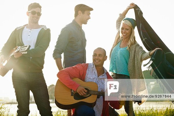 Vier erwachsene Freunde mit Akustikgitarre und Picknickdecke am Bournemouth Beach  Dorset  UK