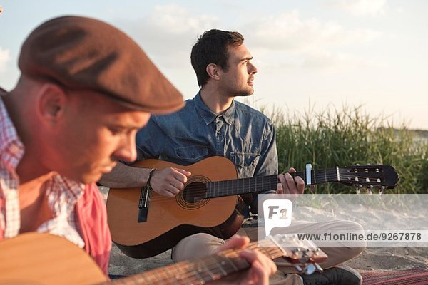 Zwei erwachsene männliche Freunde spielen Akustikgitarren am Bournemouth Beach  Dorset  UK