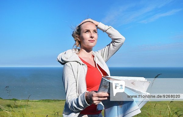 Young woman holding map by sea