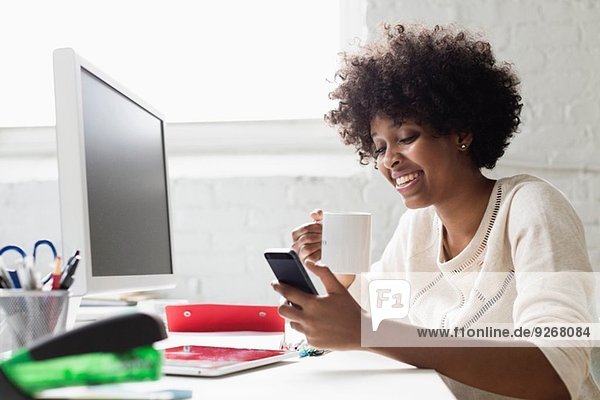 Junge Frau am Schreibtisch mit Kaffee über Smartphone