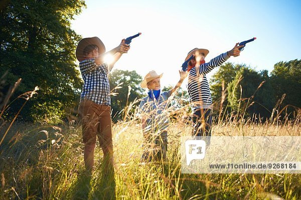 Drei kleine Jungen als Cowboys verkleidet  die Spielzeugwaffen halten.