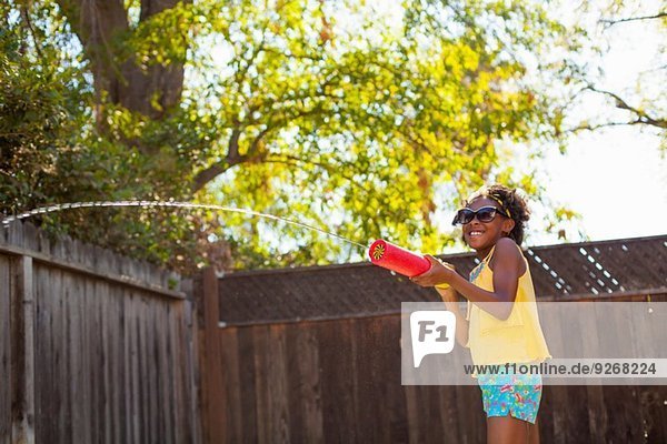 Mädchen spritzt Wasser aus Wasserpistole im Garten