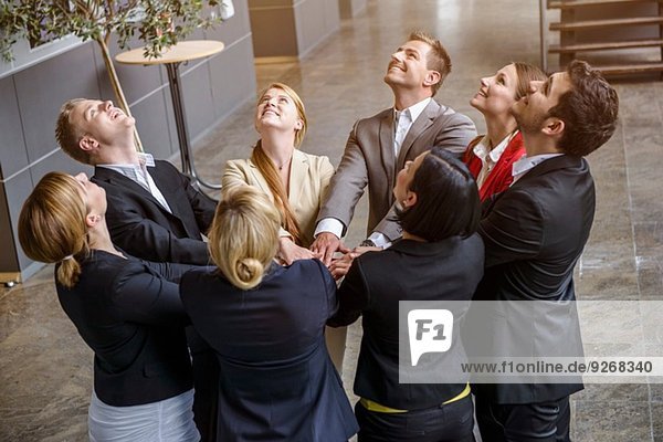 Group of businesswomen and men looking up with hands together in a circle