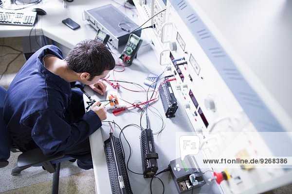 High angle view of male electrician repairing electronic equipment in workshop
