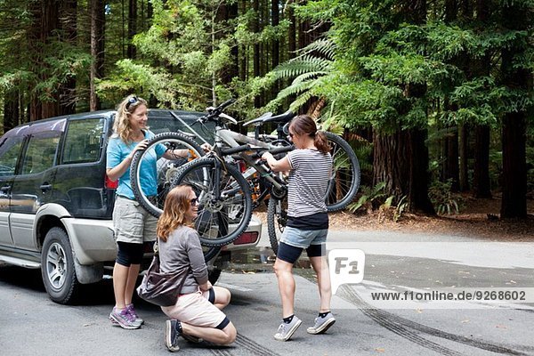 Three women mountain bikers lifting bikes from four wheel vehicle in forest