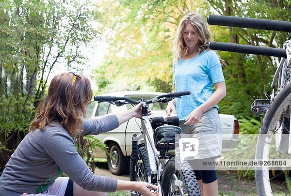 Two women mountain bikers checking cycles in forest
