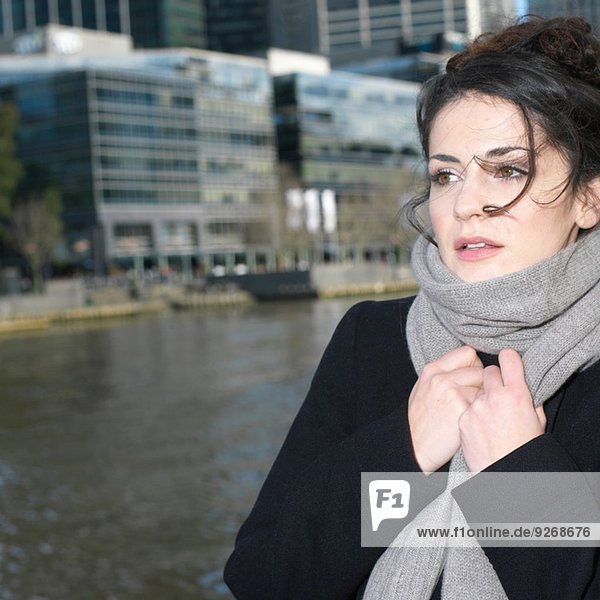 Junge Frau hält sich an gewickeltem Schal am Flussufer der Stadt fest
