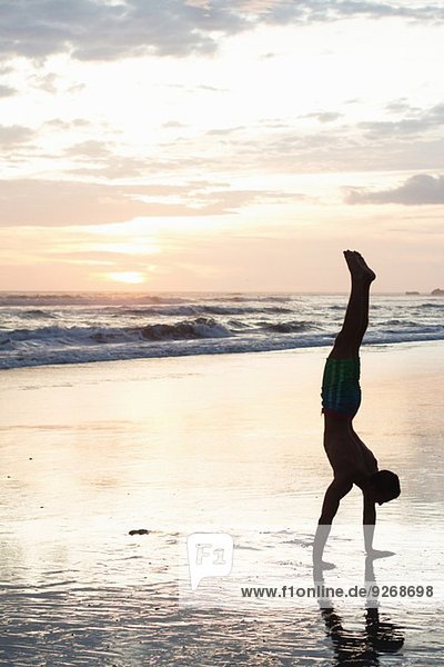 Junger Mann beim Handstand am Strand bei Sonnenuntergang  Nosara  Guanacaste  Costa Rica