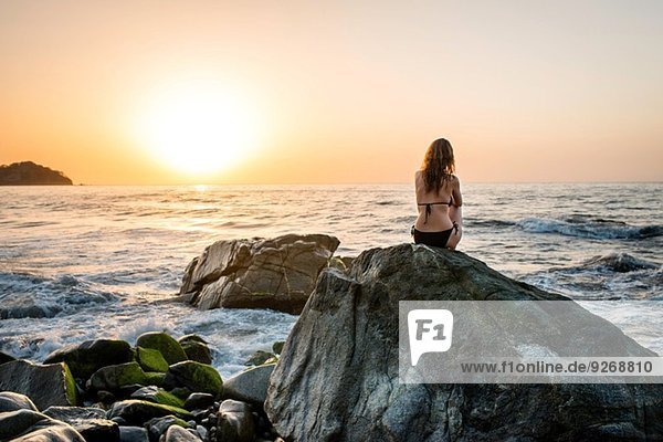 Junge Frau auf Felsen im Meer sitzend  Rückansicht