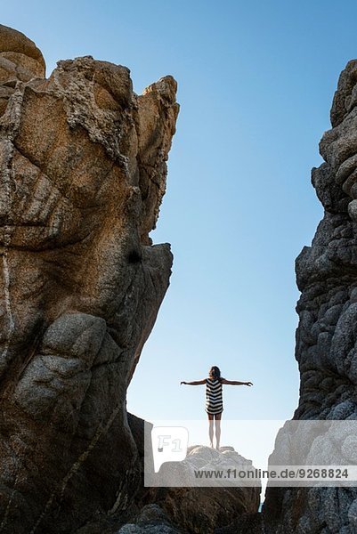 Junge Frau auf Felsen am Strand stehend  Arme ausgestreckt