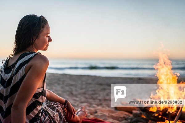 Junge Frau sitzend am Lagerfeuer am Strand