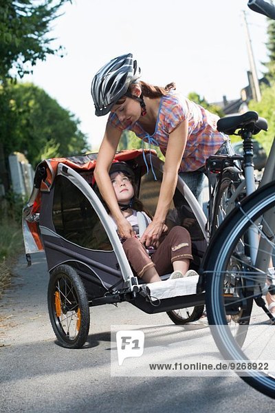 Mother fastening daughter's seatbelt in bicycle trailer