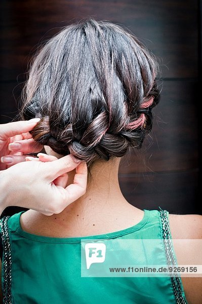 Rückansicht der Friseurin beim Flechten der Haare einer jungen Frau im Friseursalon