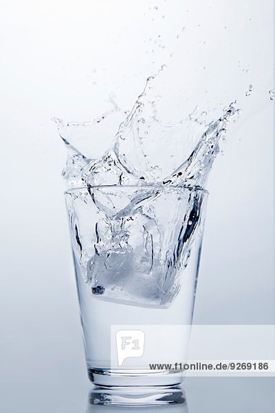 Eiswürfel  der in ein Glas mit klarem Wasser spritzt.