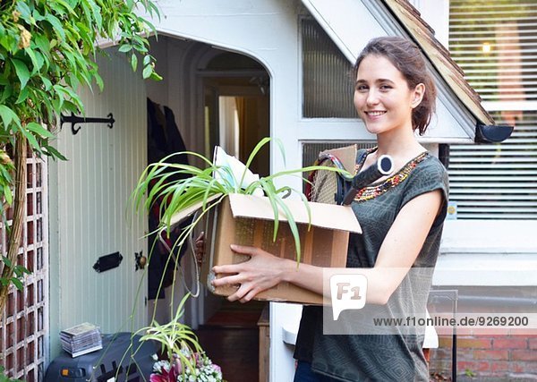 Junge Frau vor neuem Haus mit Pappkarton