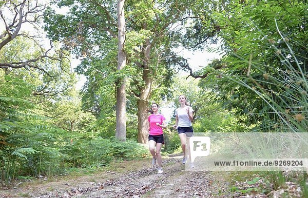 Two young women runners running through forest track