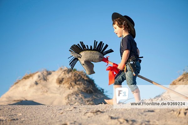 Junge als Cowboy verkleidet mit Hobbypferd in Sanddünen