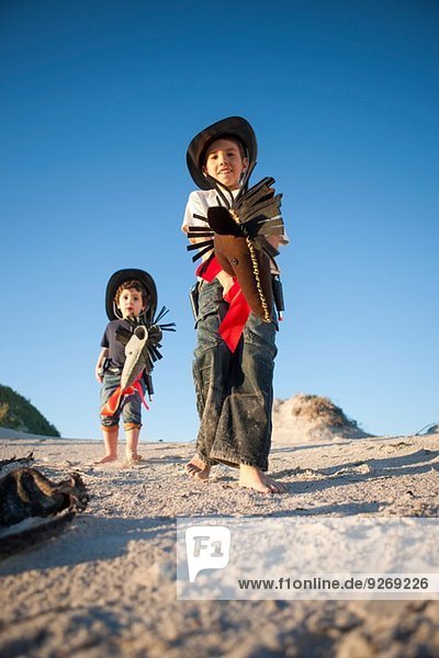 Tiefblick auf zwei Brüder als Cowboys mit Hobbypferden in Sanddünen verkleidet