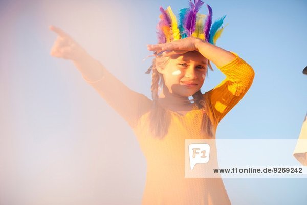 Mädchen gekleidet als Indianerin in Federkopfschmuck mit Handschattenaugen und Zeigefinger