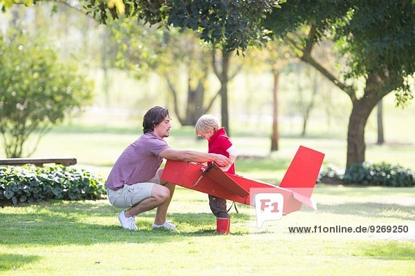 Vater kauert  um Spielzeugflugzeug für seinen Sohn im Park vorzubereiten.
