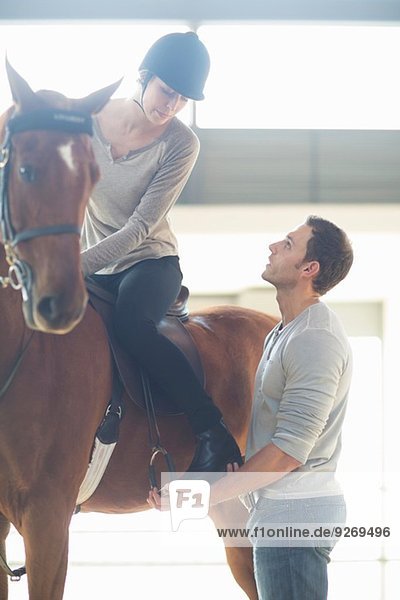 Female horseback rider with instructor in indoor paddock