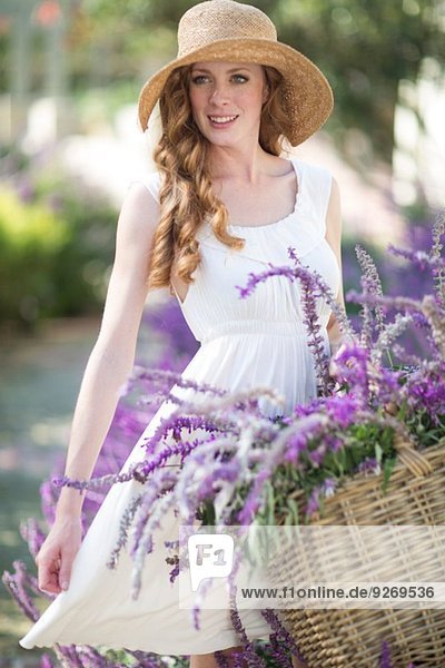 Porträt einer schönen jungen Frau im Garten mit einem Korb mit violetten Blumen