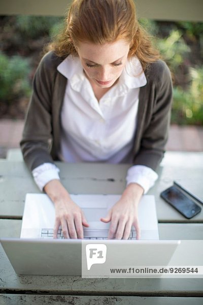 Junge Geschäftsfrau beim Tippen am Laptop am Gartentisch