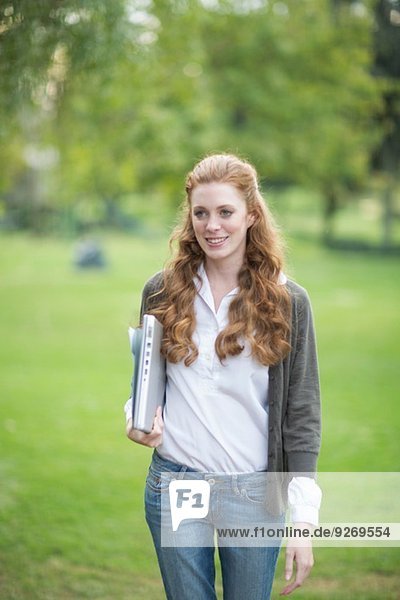 Young woman carrying laptop and walking in park