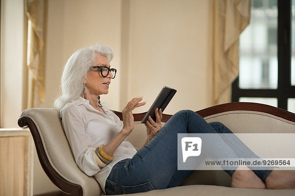 liegend liegen liegt liegendes liegender liegende daliegen Senior Senioren benutzen Frau Couch Tablet PC zurücklehnen