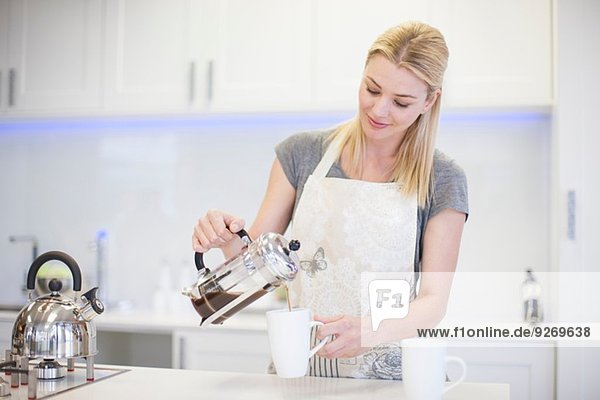 Junge Frau gießt Kaffee aus französischer Presse in die Küche