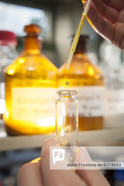 Eine Laborantin füllt mit einer Pipette eine chemische Flüssigkeit in einen Glasbehälter