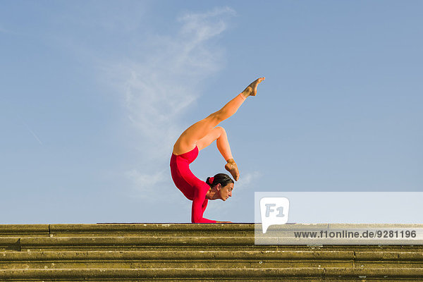 Junge Frau praktiziert Hatha-Yoga im Freien  in Vrischikasana-Haltung  Skorpion-Pose