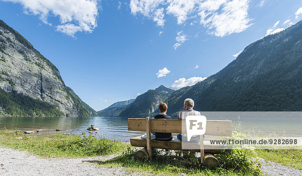 Zwei Personen sitzen auf Bank  blicken über den Königssee  St. Bartholomä am Königssee  Nationalpark Berchtesgaden  Berchtesgadener Land  Oberbayern  Bayern  Deutschland