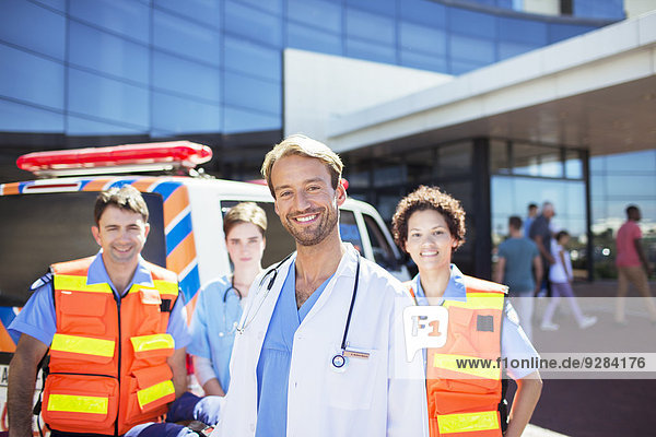Arzt lächelt mit Sanitätern auf dem Krankenhausparkplatz
