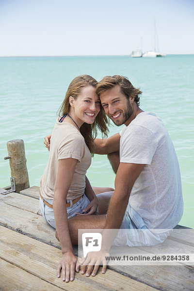 Couple sitting on edge of wooden dock together