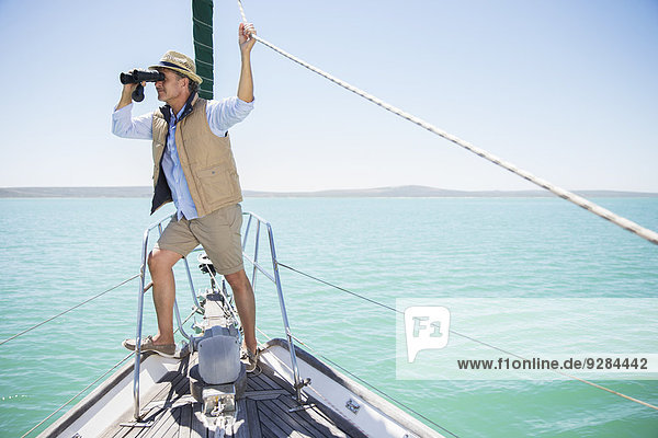 Older man looking out binoculars on edge of boat