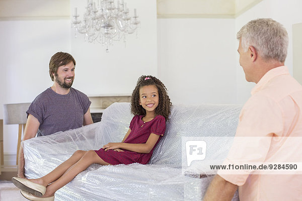 Family carrying couch with young girl sitting on top