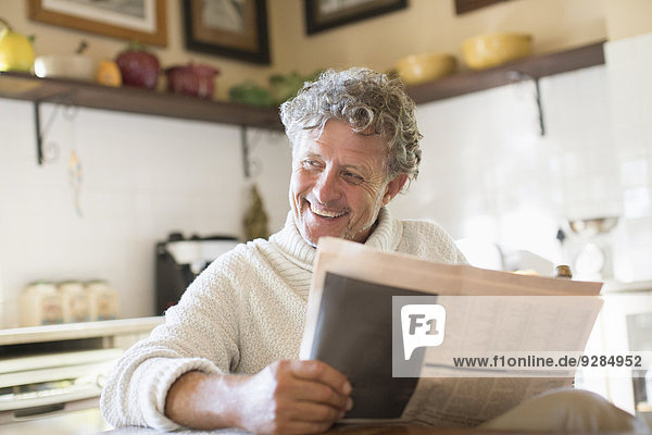 Älterer Mann liest Zeitung in der Küche