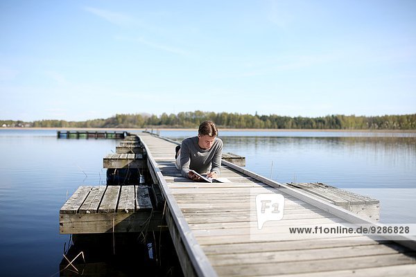 Young man on jetty reading book