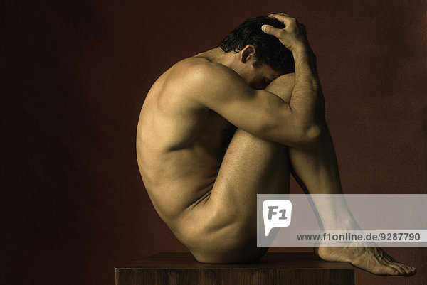 Nackter Mann sitzt in fetaler Position  Hände auf dem Kopf  Seitenansicht