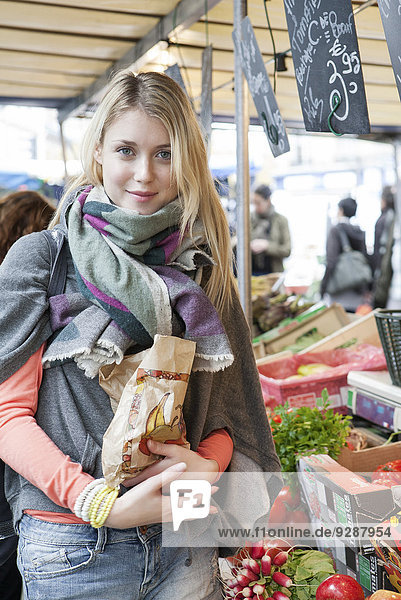 Junge Frau beim Gemüsehändler  die frisches Obst und Gemüse kauft.